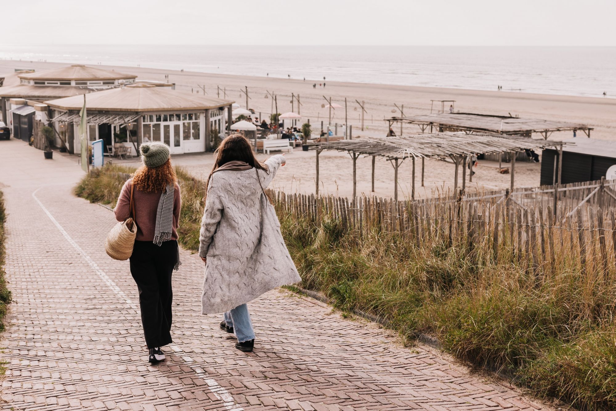 Twee wandelaars in winterjas lopen over het duinpad naar NIUS Beach House, met het strand en de zee erachter