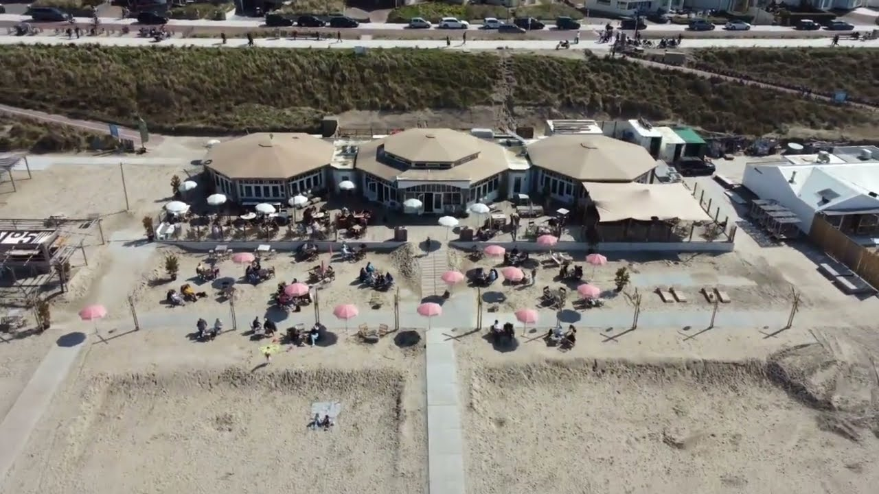 NIUS Beach House van bovenaf: drie ronde gebouwen naast elkaar, met terrassen ervoor en een terras met parasols op het zand