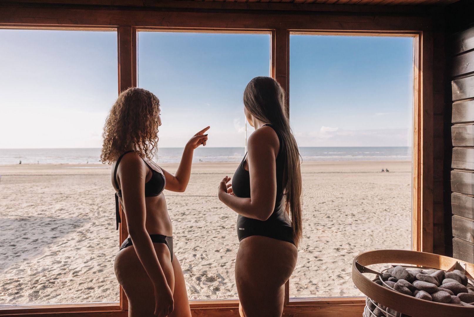 Blick aus der Billies Sauna: durch das große Fenster Strand und Meer, daneben der Ofen mit Steinen