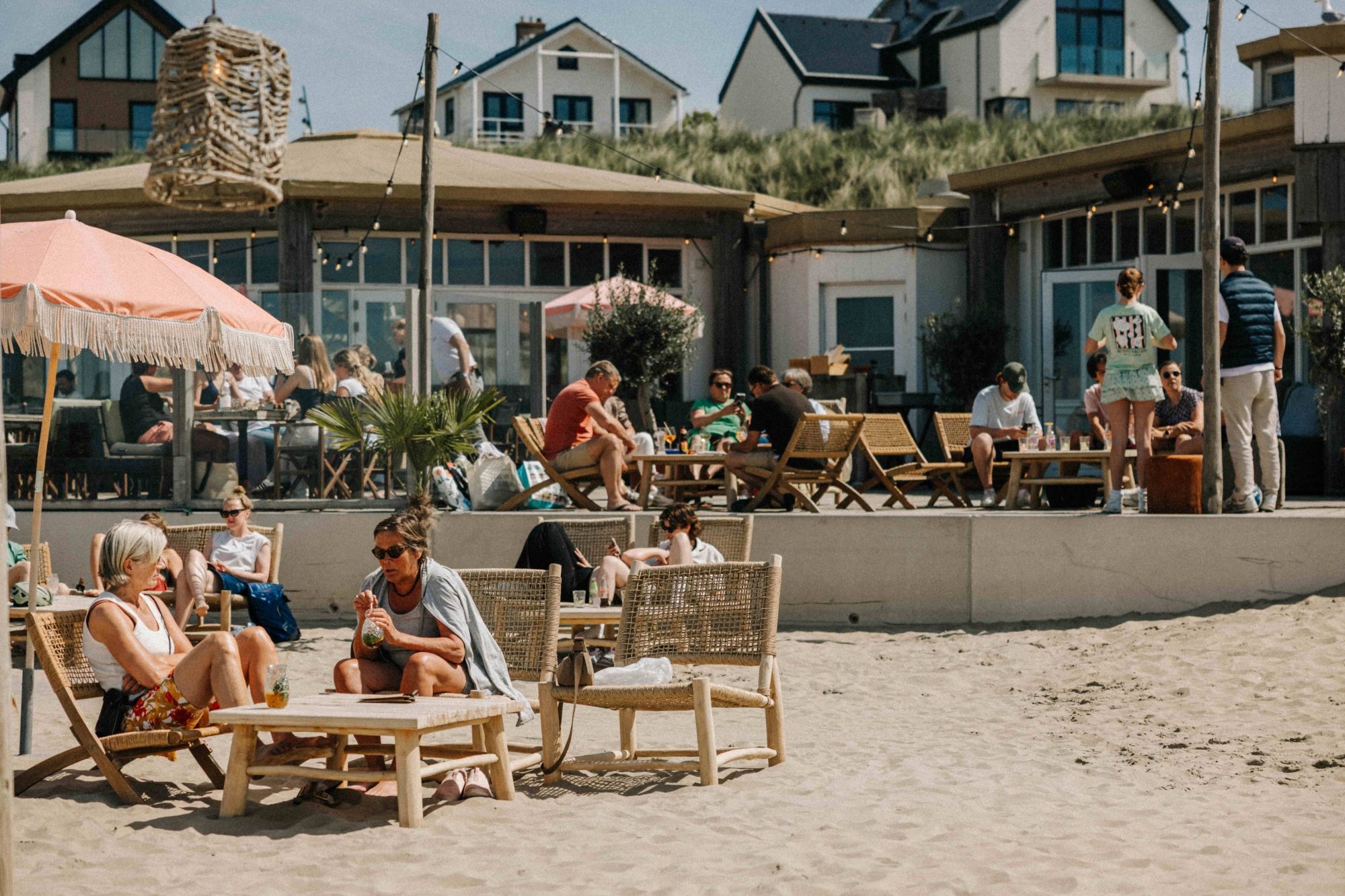 Gasten in strandstoelen op het zand voor NIUS Beach House